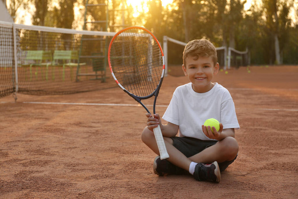 Cute little boy with tennis racket and ball on court outdoors - Фото, зображення