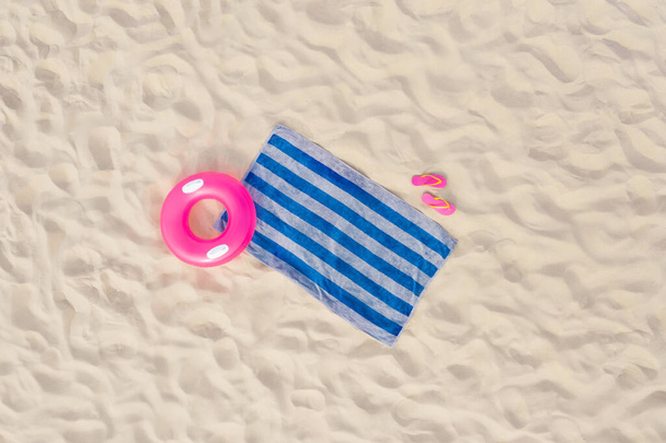 Striped beach towel, flip flops and swim ring on sand, aerial view - Zdjęcie, obraz