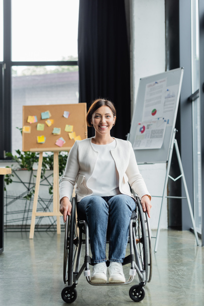felice donna d'affari con disabilità fisica vicino a lavagna a fogli mobili sfocati e sughero in ufficio - Foto, immagini