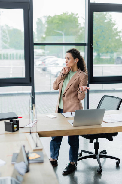 attente Afrikaans-Amerikaanse zakenvrouw in oortelefoon wijzen naar laptop tijdens videoconferentie in het kantoor - Foto, afbeelding