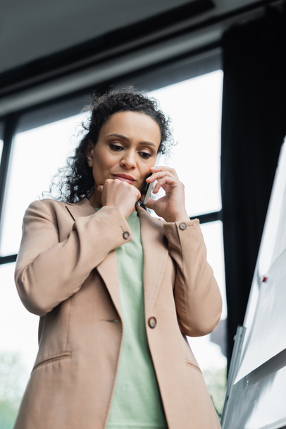Niedrigwinkel-Ansicht einer besorgten afrikanisch-amerikanischen Geschäftsfrau, die im Büro mit dem Handy telefoniert - Foto, Bild