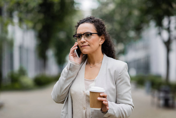 Nervöse afrikanisch-amerikanische Geschäftsfrau mit Imbissgetränk telefoniert auf der Straße - Foto, Bild
