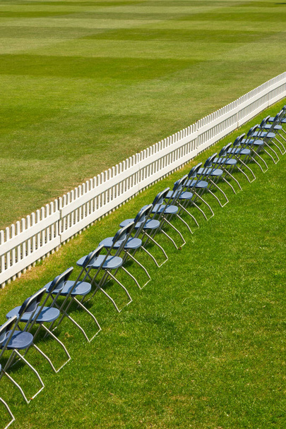Neat row of chairs and white picket fence on cricket ground - Photo, Image