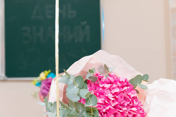 Kytice krásných jasných květin na školním stole 1. září. Nápis na školní radě je Den poznání. Selektivní soustředění. Detailní záběr - Fotografie, Obrázek