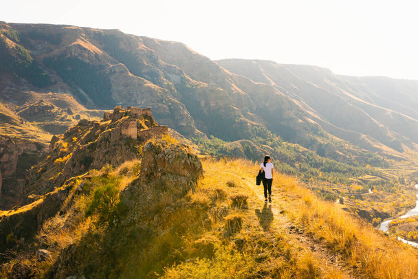 Donna cammina sulla collina verso la fortezza Tmogvi circondato da una natura dorata autunno e paesaggio drammatico in caucaso. - Foto, immagini