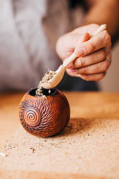 Mate cooking - Closeup of a female hand sprinkles dried mate leaves in a calabash with a wooden spoon - Foto, immagini