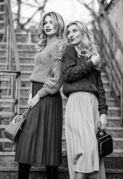 Matching colors. Personal stylist service. Sweater skirt trend. Completing each other. Matching outfits. Women sisters outdoors stairs background. Vogue concept. Girls blonde wear matching clothes - Foto, immagini