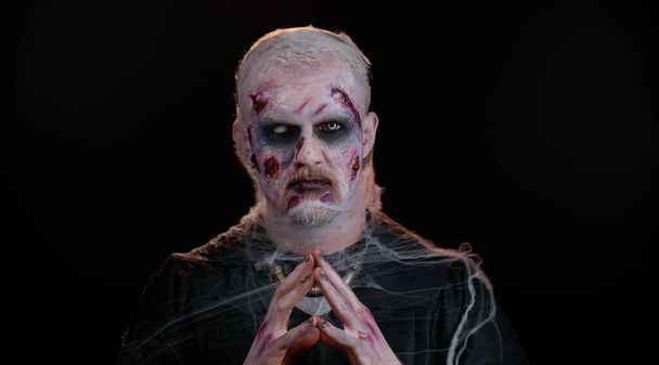 Frightening man with Halloween zombie bloody wounded makeup, trying to scare, praying, horror theme - Photo, Image