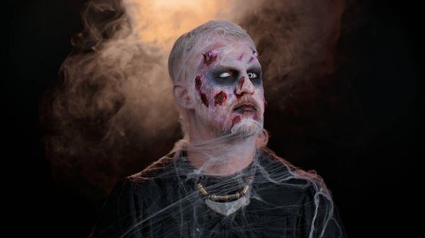 Sinister man in costume of Halloween crazy zombie with bloody wounded scars face screaming, shouting - Photo, Image