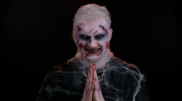 Хитрый зловещий человек в костюме зомби на Хэллоуин с окровавленным раненым лицом, пытающийся напугать - Фото, изображение