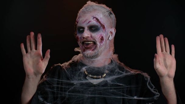 Yaralı suratlı, kulaklık takan, müzik dinleyen, dans eden, kutlama yapan zombi Cadılar Bayramı adamı. - Fotoğraf, Görsel