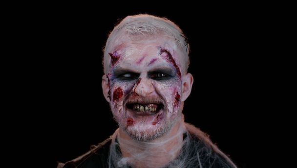 Μοχθηρός άνθρωπος με κοστούμι του Halloween τρελό ζόμπι με αιματηρές πληγωμένες ουλές πρόσωπο προσπαθεί να τρομάξει - Φωτογραφία, εικόνα