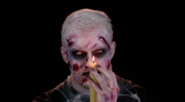 Mann mit Halloween-Zombie blutig verletzt Make-up, versucht zu erschrecken, Zauber zaubert über eine Kerze - Foto, Bild
