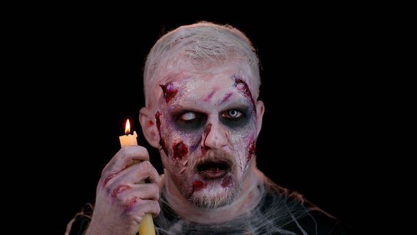 Man alleen met Halloween zombie bloederige gewonde make-up, proberen te schrikken betovert bezweringen over een kaars - Foto, afbeelding