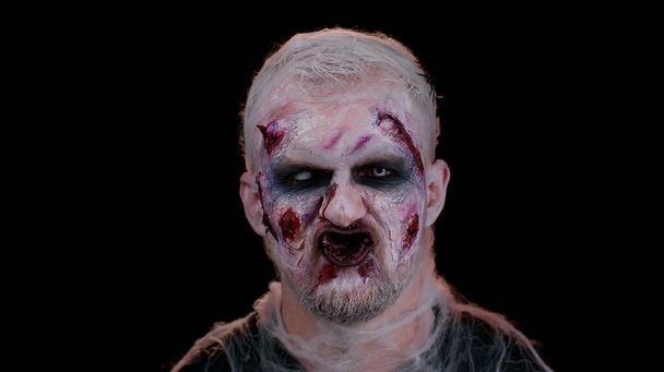 Зловещий человек с ужасной страшной зомби-макияж Хэллоуина в конвульсиях делает лица, пытаясь напугать - Фото, изображение
