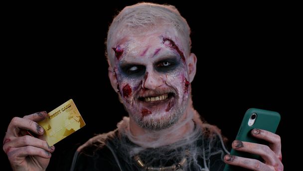 Złowieszczy człowiek Halloween zombie przy użyciu karty kredytowej i smartfona podczas zakupów online - Zdjęcie, obraz