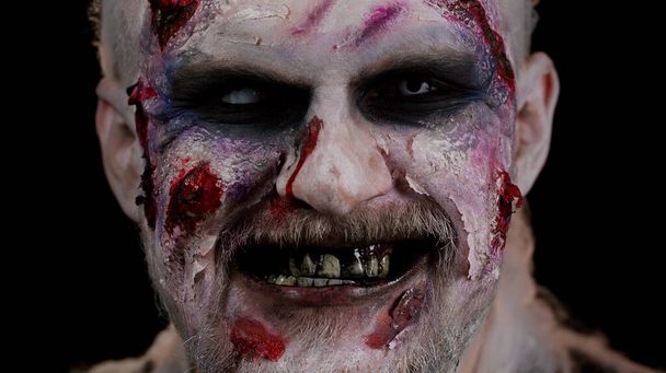 Моторошний чоловік страшно поранений криваві шрами обличчя Хеллоуїн неживий хлопець дме дим з носа, посміхається
 - Фото, зображення