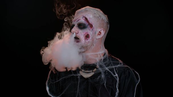 Creepy man scary wounded bloody scars face Halloween undead guy blows smoke from nose, smiles - Photo, Image