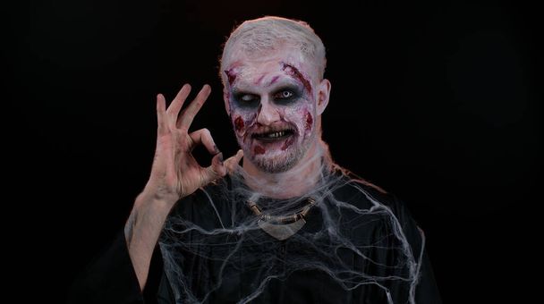 Creepy man Halloween zombie showing Ok gesture, like sign positive something good, smiles terribly - Photo, Image