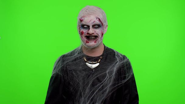 Enge griezelige man Halloween zombie trekken gezichten, kijkt naar de camera, glimlacht vreselijk met vuile tanden - Foto, afbeelding