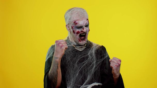 Zombie asustadizo hombre de Halloween celebrar el éxito ganar grito se regocija haciendo gesto manos ganadoras decir Sí - Foto, Imagen