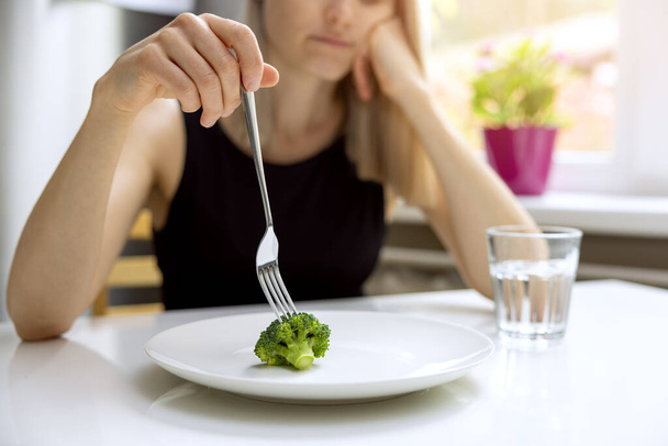 dietní problémy, porucha příjmu potravy - nešťastná žena při pohledu na malé porce brokolice na talíři - Fotografie, Obrázek