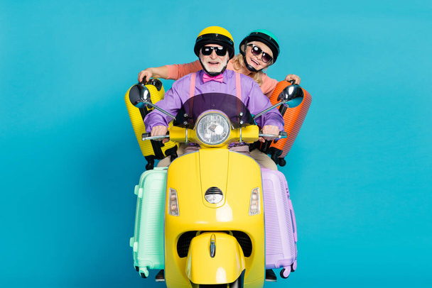 Photo of grey haired married couple retired pensioner wear helmet sunglass hold bags biker isolated on blue color background - Foto, immagini