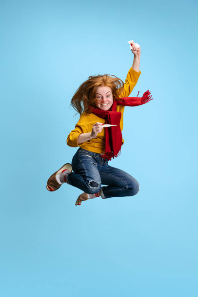 Pionowy ortret młodej podekscytowanej dziewczyny w skoku odizolowanym na niebieskim tle. Odzyskiwanie spalin, zimno - Zdjęcie, obraz