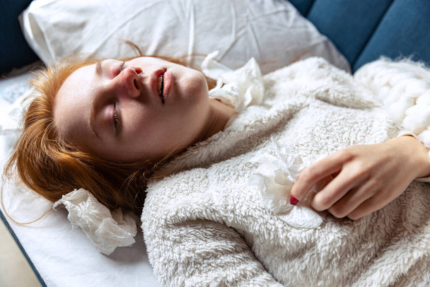 Zastřižený portrét mladé nemocné dívky s červeným nosem ležící na pohovce. Špatný pocit - Fotografie, Obrázek