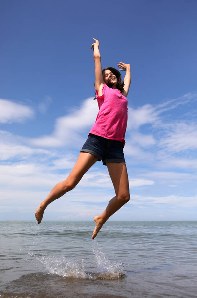 Sprung eines glücklichen kaukasischen Mädchens an der Küste im Sommer Symbol der Freude und Unbekümmertheit am Strand - Foto, Bild