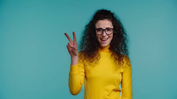 amazed young woman in glasses showing peace sign isolated on blue  - Photo, Image