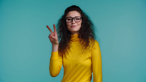 šťastná mladá žena v brýlích ukazující mír znamení izolované na modré  - Fotografie, Obrázek