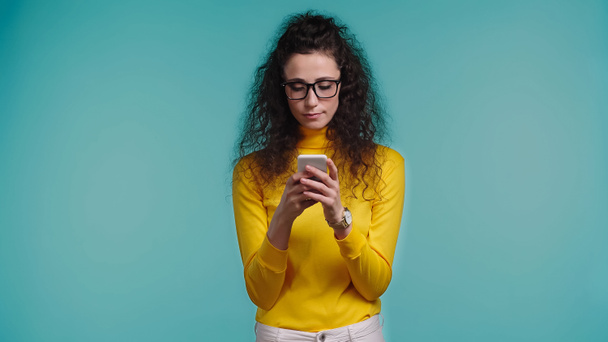 mladá žena v brýlích pomocí smartphone izolované na modré  - Fotografie, Obrázek