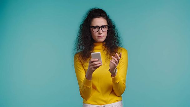 fiatal nő szemüvegben gazdaság okostelefon elszigetelt kék  - Fotó, kép