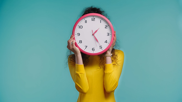 young woman obscuring face with wall clock isolated on blue - Φωτογραφία, εικόνα