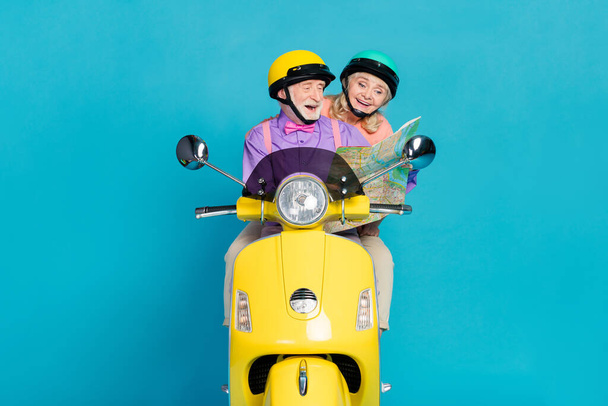 Portrait of two cheerful elderly retired pensioner friends riding moped reading map isolated over bright blue color background - Photo, Image
