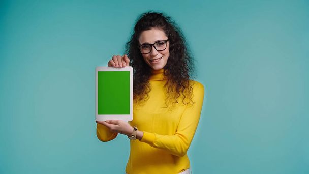 happy woman in glasses holding digital tablet with green screen isolated on blue - Foto, Imagen