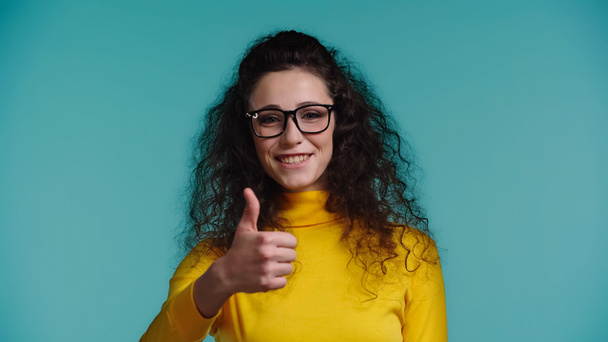 young woman in glasses smiling while showing thumb up isolated on blue  - Fotografie, Obrázek
