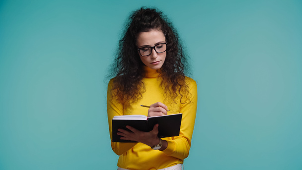 young woman in glasses and turtleneck holding notebook and pen isolated on blue  - Photo, Image