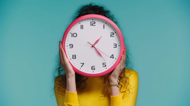 woman obscuring face with wall clock isolated on blue - Foto, Imagen