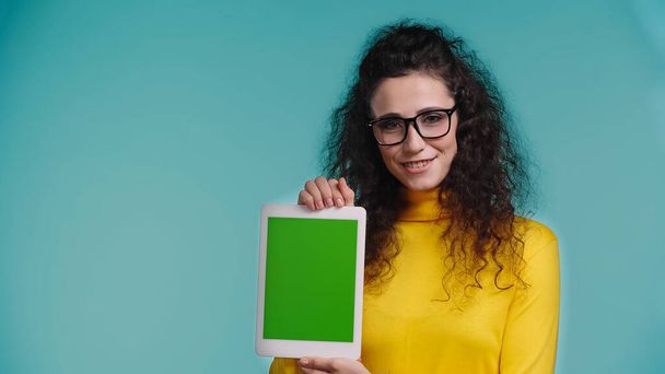 pozitivní žena v brýlích drží digitální tablet se zelenou obrazovkou izolované na modré  - Fotografie, Obrázek