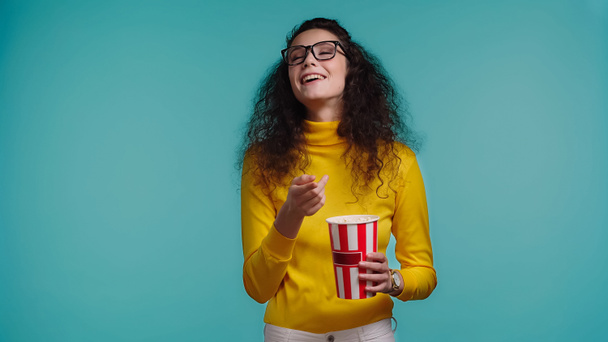 szczęśliwy młody kobieta trzyma popcorn wiadro i oglądać film odizolowany na niebieski   - Zdjęcie, obraz