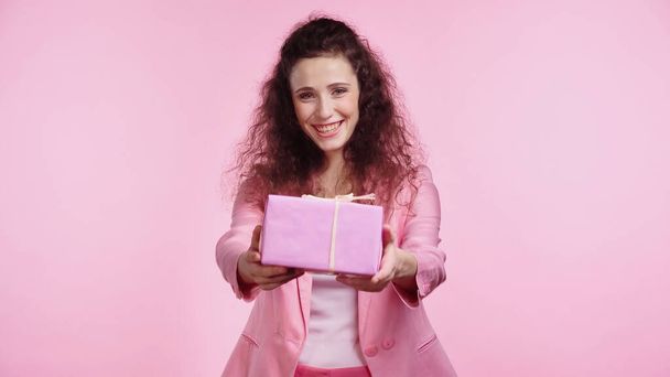 brunette and happy young woman looking at camera while holding present isolated on pink  - Foto, Imagem