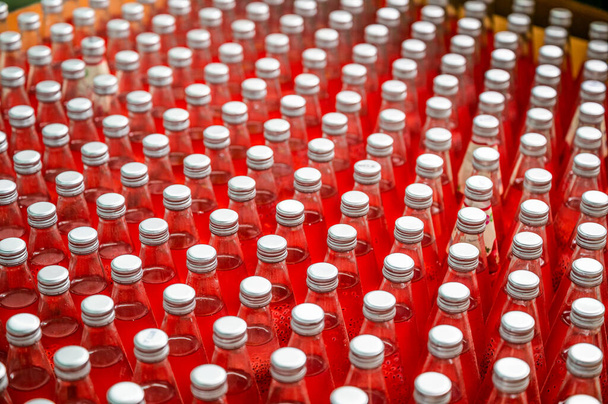 Piros lé flakonok csoportja csavaros kupakkal a szállítószalagban az italfeldolgozó üzemben - Fotó, kép