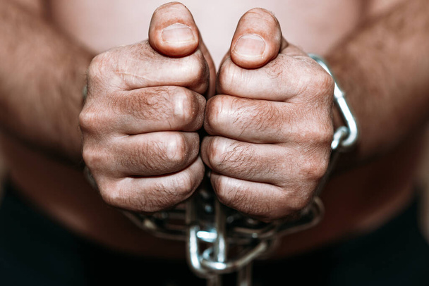 Покаявшийся заключенный с руками, закованными в цепи на темно-сером фоне.. - Фото, изображение