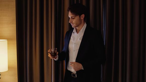 confident businessman holding glass of whiskey in hotel room - Foto, afbeelding
