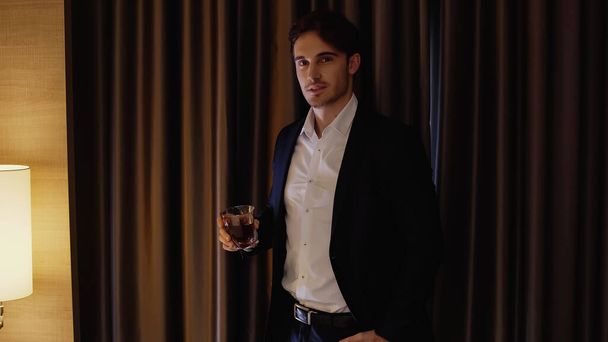 good-looking businessman holding glass of whiskey in hotel room - Fotó, kép