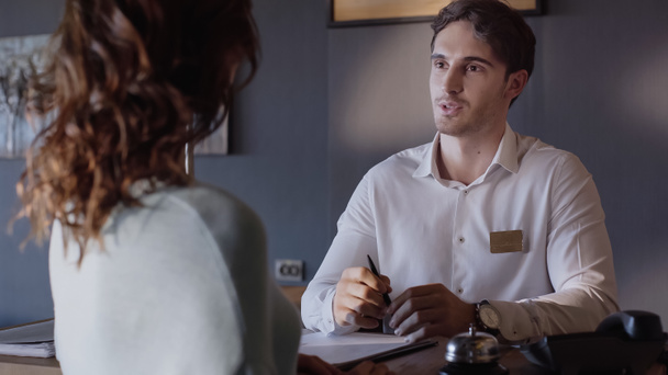 young hotel receptionist talking with blurred client at hotel counter  - Photo, image