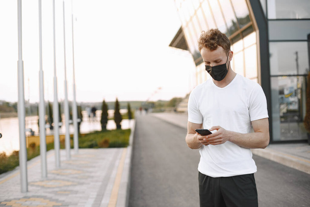 Portrait of a young fit man in a face mask jogging outdoors on a stadium - 写真・画像