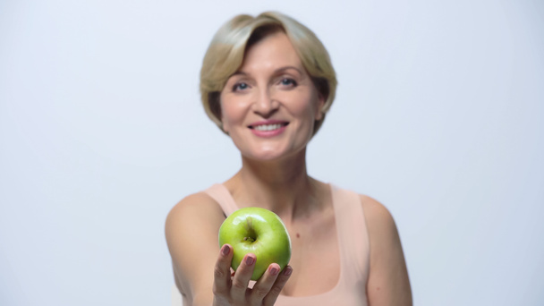 borrosa mujer de mediana edad mostrando manzana verde y sonriendo a la cámara aislada en blanco - Foto, Imagen